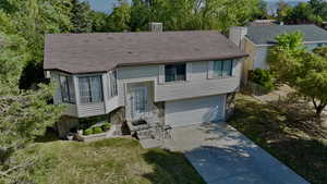 Bi-level home featuring driveway, roof with shingles, a garage, and a front yard