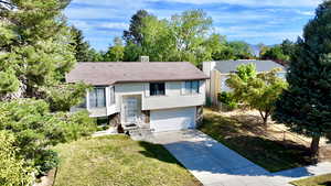 Raised ranch with driveway, a garage, view of wooded area, and a shingled roof