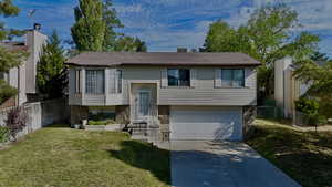 Bi-level home featuring driveway, an attached garage, and stone siding