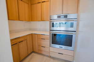 Kitchen with modern cabinets, stainless steel double oven, light brown cabinets, light stone countertops, and light tile patterned flooring