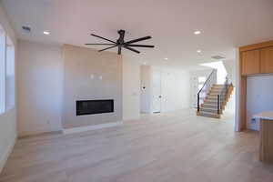 Unfurnished living room featuring stairs, a fireplace, ceiling fan, recessed lighting, and light wood-style floors