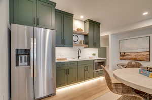 Kitchen with green cabinetry, stainless steel appliances, open shelves, light wood-style flooring, and recessed lighting