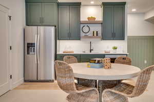 Kitchen featuring green cabinets, stainless steel fridge, open shelves, light wood finished floors, and recessed lighting