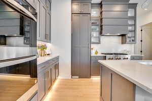 Kitchen with stainless steel appliances, light stone counters, decorative backsplash, and light wood-style flooring