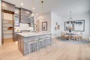 Kitchen with gray cabinets, a breakfast bar, hanging light fixtures, light wood-style floors, and recessed lighting
