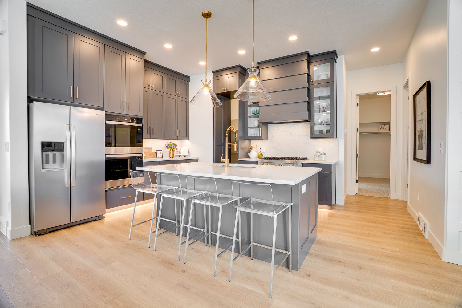 Kitchen with gray cabinetry, a breakfast bar area, decorative light fixtures, a kitchen island with sink, and appliances with stainless steel finishes