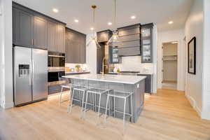 Kitchen with gray cabinetry, a breakfast bar area, decorative light fixtures, a kitchen island with sink, and appliances with stainless steel finishes