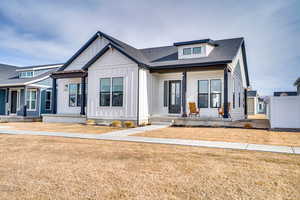 Modern farmhouse with board and batten siding, covered porch, a shingled roof, and a front lawn