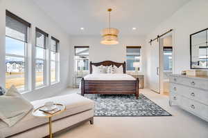 Bedroom with a barn door, light carpet, recessed lighting, and ensuite bathroom