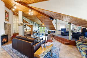 Living area featuring a wooden ceiling with exposed beams, a tiled fireplace, high vaulted ceiling, rail lighting, and ceiling fan