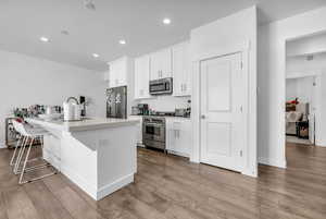 Kitchen featuring a breakfast bar, white cabinetry, high quality appliances, an island with sink, and light wood-style floors