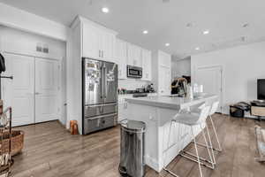 Kitchen with white cabinets, appliances with stainless steel finishes, a breakfast bar, light wood finished floors, and recessed lighting