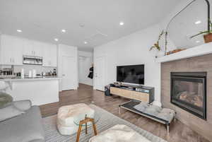Living room with light wood-type flooring, recessed lighting, a tiled fireplace, and attic access