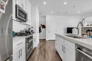 Kitchen with appliances with stainless steel finishes, white cabinetry, recessed lighting, dark wood finished floors, and light stone counters