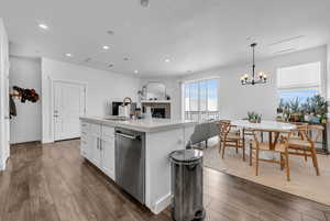 Kitchen featuring a center island with sink, white cabinetry, stainless steel dishwasher, dark wood-style flooring, and open floor plan