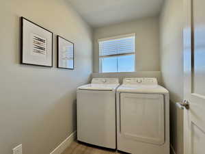 Laundry room with washing machine and clothes dryer and light wood finished floors