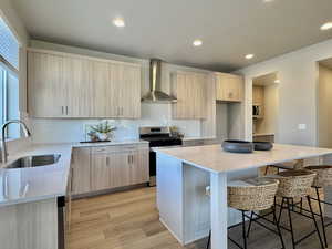 Kitchen featuring light stone counters, light brown cabinetry, stainless steel range, wall chimney range hood, and recessed lighting