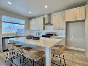 Kitchen with light stone countertops, modern cabinets, wall chimney exhaust hood, a kitchen bar, and stainless steel appliances