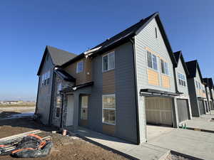 Rear view of house with a garage, roof with shingles, stone siding, and driveway