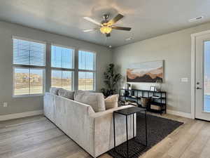 Living room featuring plenty of natural light, a ceiling fan, light wood finished floors, and a textured ceiling