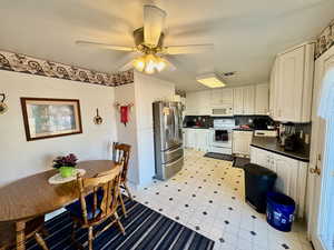 Kitchen with dark countertops, white appliances, a ceiling fan, white cabinetry, and light floors