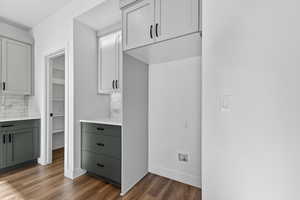 Kitchen featuring decorative backsplash, gray cabinets, dark wood-style floors, and white cabinets