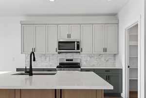Kitchen featuring light stone countertops, stainless steel appliances, backsplash, and a center island with sink