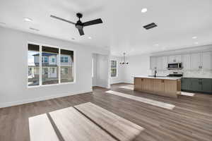 Kitchen featuring open floor plan, an island with sink, stainless steel appliances, a chandelier, and ceiling fan