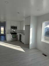 Kitchen with appliances with stainless steel finishes, white cabinetry, light countertops, light wood-type flooring, and recessed lighting