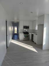 Kitchen featuring appliances with stainless steel finishes, white cabinets, light countertops, and light wood-style flooring