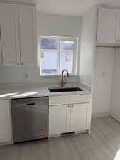 Kitchen featuring white cabinetry, stainless steel dishwasher, light wood-style flooring, and light stone counters