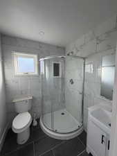 Bathroom featuring tile walls, vanity, a shower stall, and dark tile patterned flooring