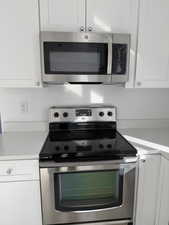 Kitchen with stainless steel appliances, white cabinetry, and light stone countertops