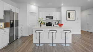 Kitchen featuring white cabinetry, stainless steel appliances, a kitchen bar, an island with sink, and recessed lighting