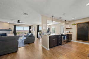 Kitchen featuring hanging light fixtures, stainless steel range with electric stovetop, open floor plan, healthy amount of natural light, and a textured ceiling