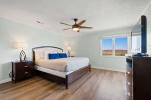 Bedroom featuring light wood-style flooring, a ceiling fan, a textured ceiling, and ornamental molding