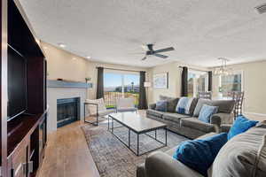 Living room featuring a fireplace, light wood-style floors, a textured ceiling, and ceiling fan