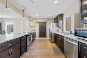 Kitchen with dark brown cabinets, appliances with stainless steel finishes, light stone countertops, a textured ceiling, and decorative light fixtures