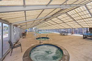 Indoor community pool featuring a community hot tub, a patio, and glass enclosure