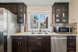 Kitchen with dark brown cabinets, glass insert cabinets, stainless steel appliances, light stone counters, and a textured ceiling