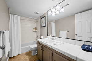 Bathroom with vanity, light tile patterned floors, shower / bath combination with curtain, and a textured ceiling