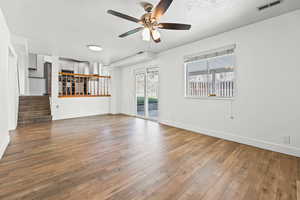 Unfurnished living room featuring ceiling fan, hardwood / wood-style floors, a textured ceiling, and stairway