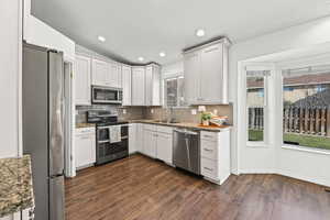 Kitchen with appliances with stainless steel finishes, light stone counters, vaulted ceiling, white cabinetry, and recessed lighting