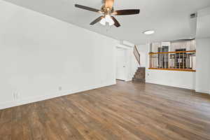 Unfurnished living room featuring hardwood / wood-style floors, ceiling fan, and stairway