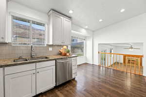 Kitchen featuring light stone counters, dishwasher, white cabinets, dark wood-type flooring, and backsplash