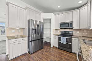 Kitchen featuring appliances with stainless steel finishes, dark stone countertops, decorative backsplash, dark wood-style floors, and recessed lighting