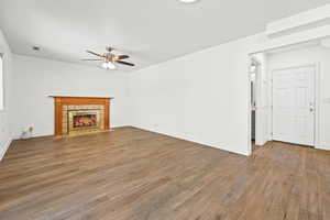 Unfurnished living room featuring light wood-type flooring, a tiled fireplace, and a ceiling fan