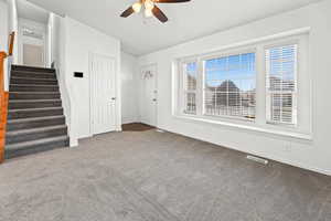 Freshly painted unfurnished living room featuring stairs, new carpeted floors, ceiling fan, and lofted ceiling
