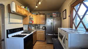 Kitchen featuring range with gas stovetop, white microwave, freestanding refrigerator, light countertops, and brown cabinetry