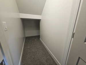 Hall featuring vaulted ceiling and dark colored carpet